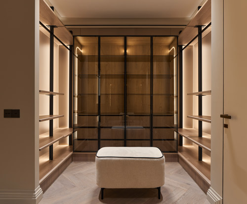 Bespoke fitted wardrobe with glass doors and shelving in a beautifully lit space